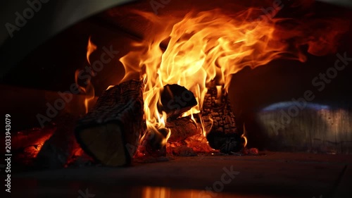 Close-up of burning logs and bright flames inside a wood-fired street food pizza oven, with warm glow, charred texture, and dark copy space