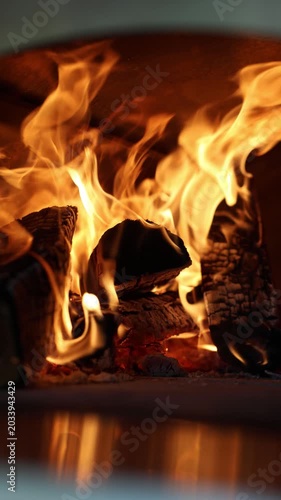 Close-up of burning logs and bright flames inside a wood-fired street food pizza oven, with warm glow, charred texture, and dark copy space