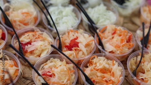Small plastic cups filled with pickled cabbage, carrot, and peppers, served with black forks at a street food market