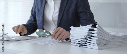 Cuadro en lienzo Professional accountant or auditor carefully examining financial documents and corporate reports with a magnifying glass, diligently researching tax obligations and legal compliance