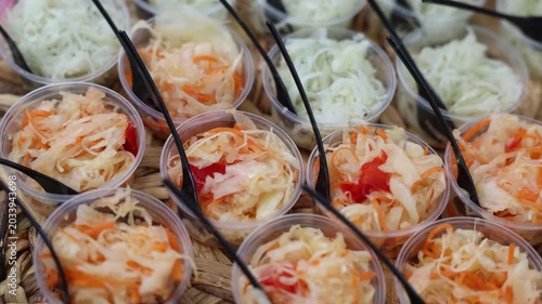 Small plastic cups filled with pickled cabbage, carrot, and peppers, served with black forks at a street food market
