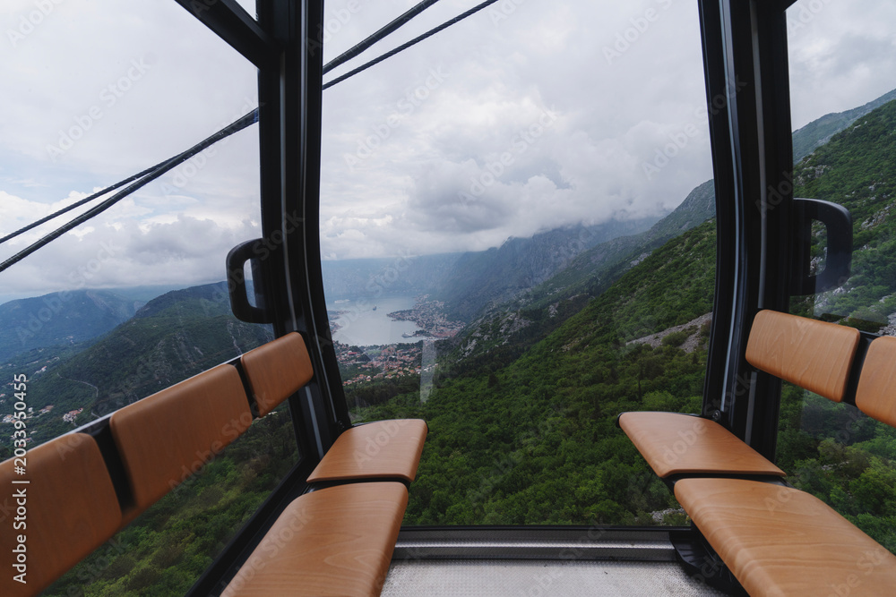 Fototapeta premium Inside view of a cable car cabin with a breathtaking panoramic outlook of mountains, sea bay, and clouds.