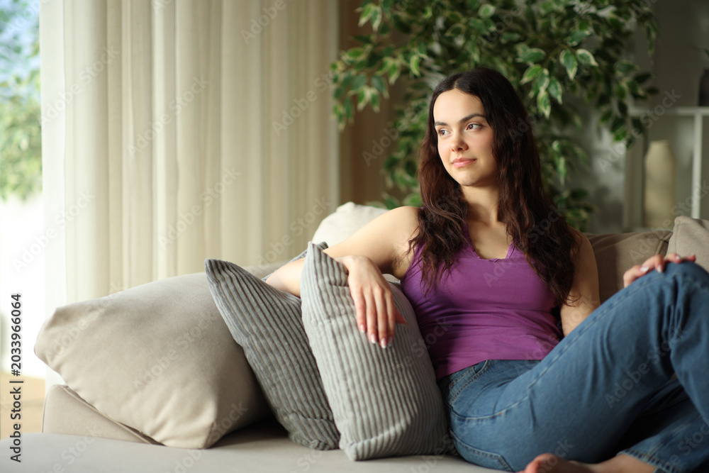 Obraz premium Relaxed young woman thinking at home contemplating through a window