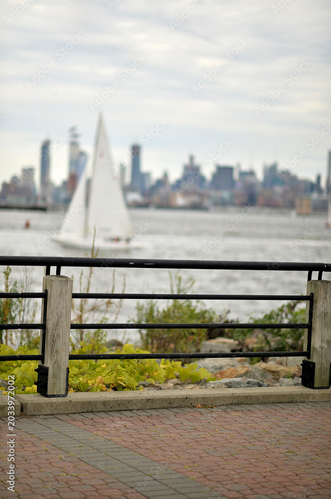 Obraz premium Small Sailboat Moves Smoothly Over Surface Of Water With Highrise Buildings In Background new york