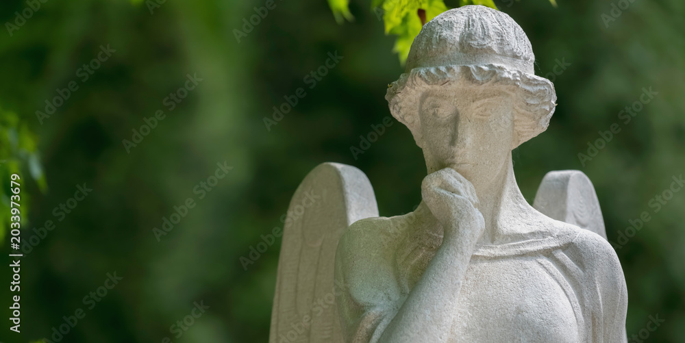 Obraz premium Thoughtful guardian angel statue in peaceful green surroundings. Copy space for text or design.