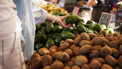 Woman selecting ripe avocado at outdoor market, supporting plant-based nutrition, vegan lifestyle, and healthy organic food choices while shopping for fresh produce.