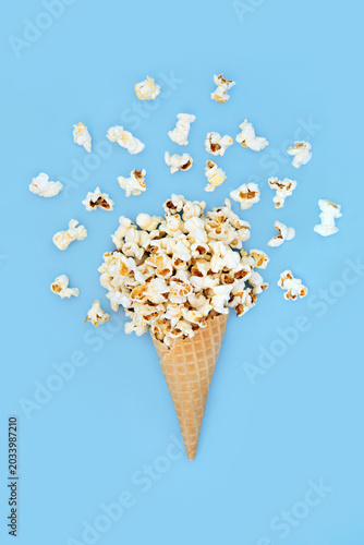 Surreal summer popcorn ice cream cornet on blue background with loose corn. Fun holiday summertime food art whimsical design.