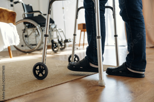 Schilderij op canvas Individual using a walker for support stands on wooden floor in a well-lit room