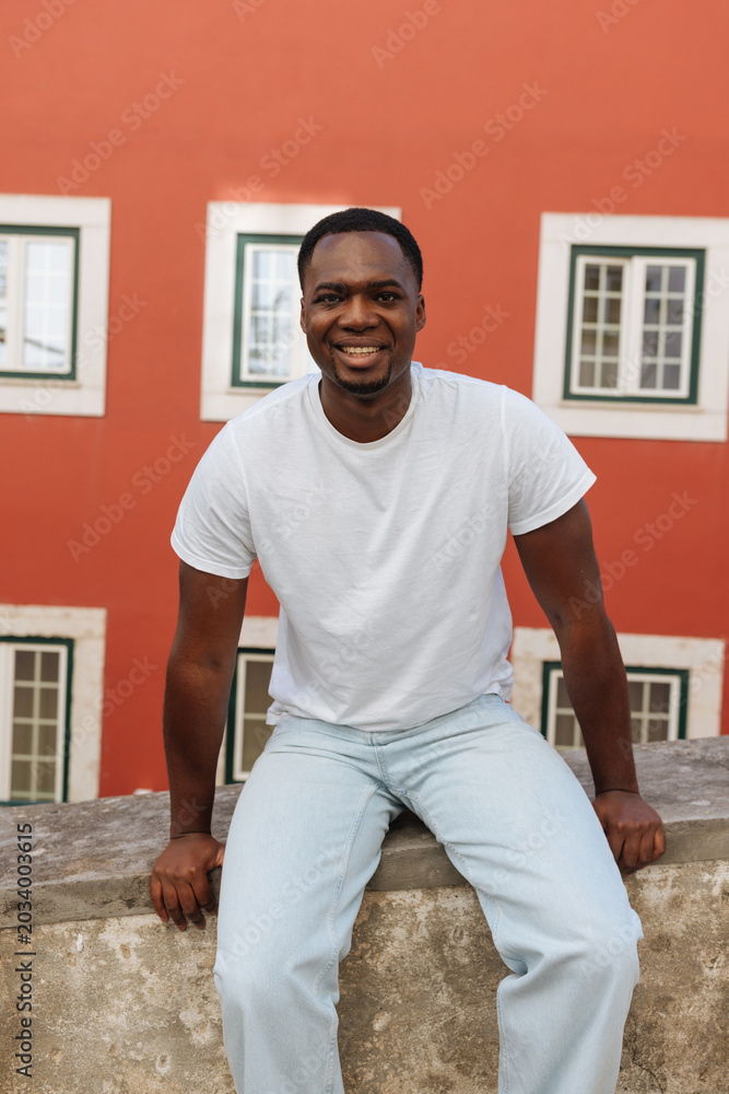 Fototapeta premium Young black man smiling outdoors, red building background
