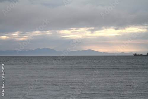 Horizontal wide scenic view of Mount Fuji silhouette under twilight clouds over the sea.