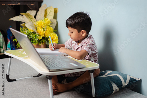 Young Indian boy focused on online learning at home with laptop and notebook