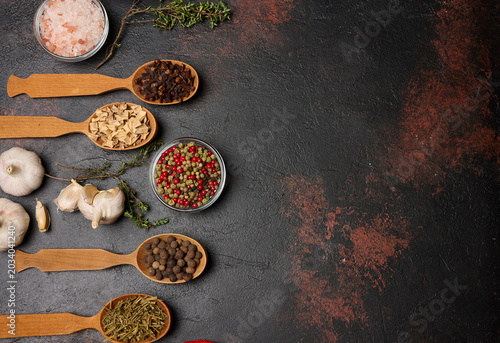 Photos Spices on a dark background in wooden spoons: pepper, cloves, ginger, allspice and bay leaf, salt, thyme
