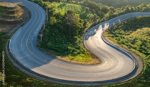 Scenic drone shot capturing a dramatic hairpin curve road surrounded by lush forest and rolling countryside in Loei Province. Winding Asphalt Road in Highlands Scenic Route Through Green Valley