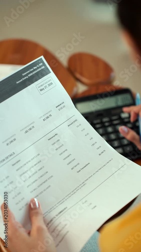 Young woman calculating household expenses and managing budget with smartphone and bills at home office desk. Personal finance, saving and financial planning concept.
