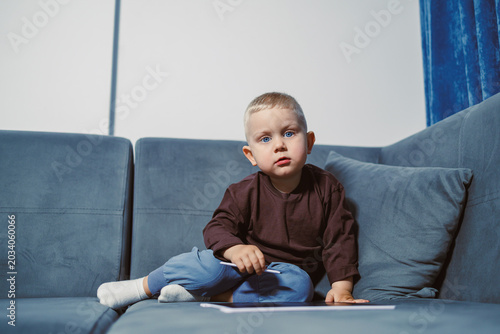 Bild auf Leinwand Small child sits on sofa and looks at camera in living room during daytime