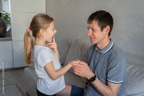 Photos Father and young daughter holding a fallen primary milk tooth in the living room