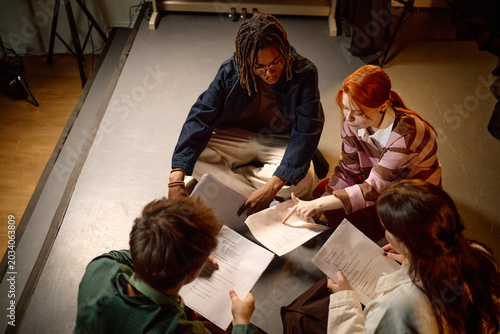 High angle view of diverse students reviewing scripts on floor, collaborating in study group or drama class. Education, teamwork, youth learning campaign or school promotion use
