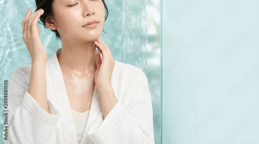 Naklejka premium 水色の保湿背景とローブ姿で首元を整える若い女性の美容ビジュアル