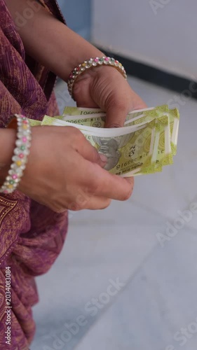 Indian woman's hands counting a stack of twenty-rupee banknotes