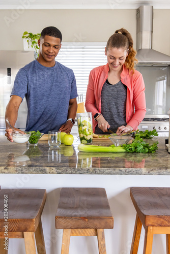Diverse couple preparing fresh ingredients at kitchen island with blender jar and cutting board