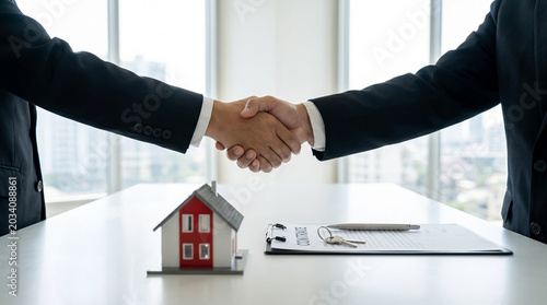 Business handshake over miniature house, symbolizing real estate contract, property investment, and successful negotiation.