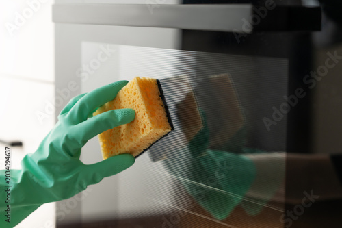 Cleaning the oven door with a sponge and a rubber glove, removing grease in a modern kitchen.