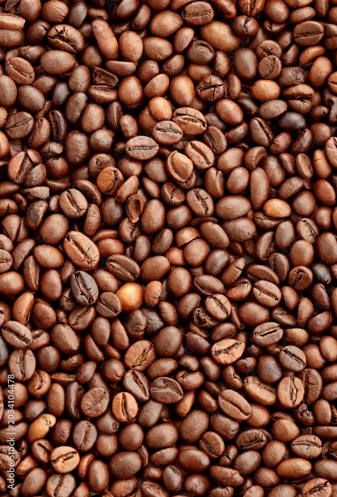 Fototapeta premium Brown roasted coffee beans in big pile on table close up. Large amount of coffee grains
