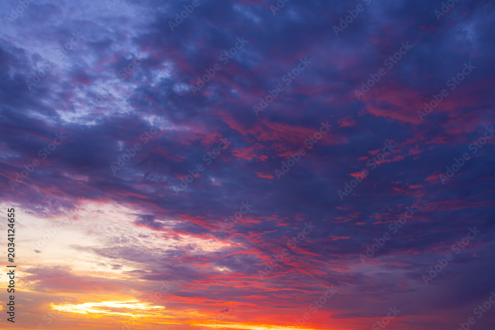 Fototapeta premium A breathtaking, vibrant sunset sky filled with dramatic, textured clouds painted in brilliant shades of fiery orange, deep magenta, and soothing twilight purple, capturing the serene beauty.