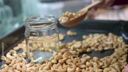 Woman pouring roasted cashew nuts into glass jar during healthy kitchen cooking video preparation HD Full