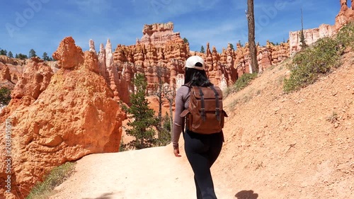 Happy young woman with a backpack hiking on the navajo loop and queen's garden trail in bryce canyon national park, utah, enjoying the spectacular hoodoos rock formations on a sunny day