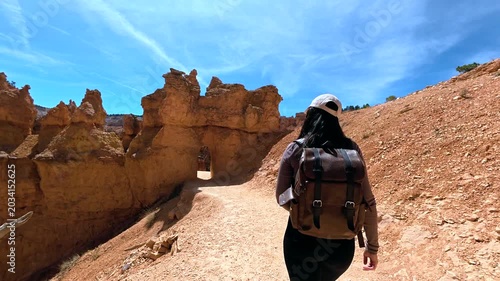 Adventurous young female photographer hiking the navajo loop and queen's garden trail, walking through unique rock formations in bryce canyon national park, utah, on a sunny day