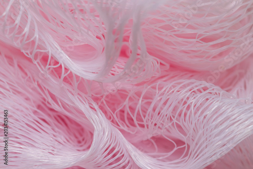Macro shot of pink mesh shower puff or bath sponge. Close up abstract background of soft synthetic net texture for hygiene, body care, and bathroom concepts.