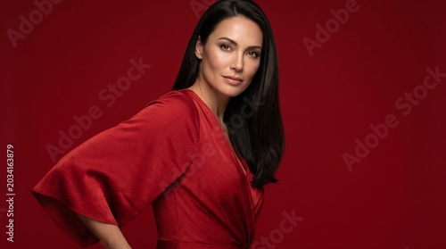 Elegant woman with dark hair wearing a red dress against a crimson background, studio portrait