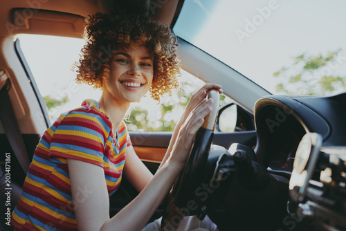 Quadro su tela Bright outdoor moment with a smiling woman behind the wheel in a striped shirt,