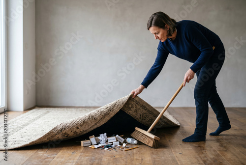 Eine Frau kehrt Probleme unter den Teppich, Redewendung „etwas unter den Teppich kehren“