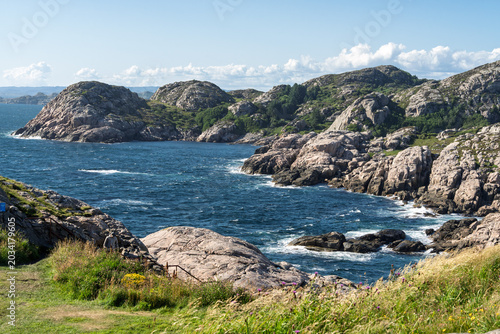 Wave exposed North Sea coastline with rugged granite shore, breaking waves and weathered rock formations near Lindesnes Lighthouse in southern Norway for marine tourism and coastal geography