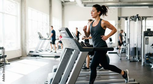 Young woman running on a treadmill in a modern gym. Female athlete doing cardio workout for stamina and weight loss. Fitness and health concept