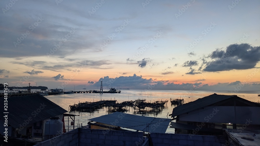 Fototapeta premium Beautiful sunset over a peaceful harbor with colorful sky reflections, calm ocean water, and dramatic clouds during twilight