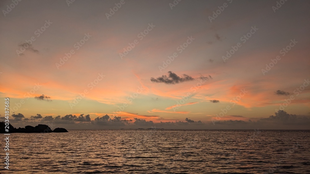 Fototapeta premium Colorful tropical ocean sunset with calm sea waves and soft clouds glowing in orange and pink evening light.
