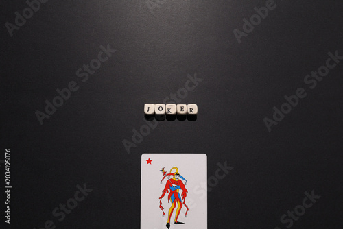 Foto Joker spelled with letter tiles above a joker playing card on dark background, representing wildcard, unpredictability, chaos and risk