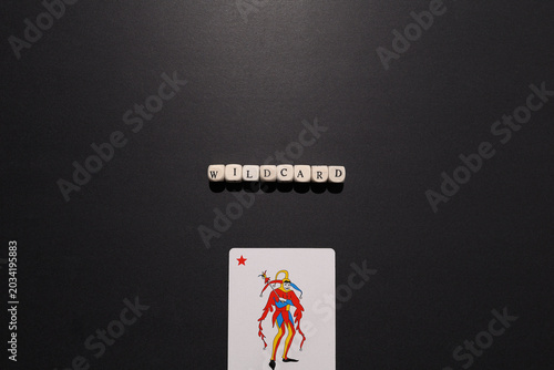 Foto Wildcard spelled with letter tiles above a joker card on dark textured background, symbolizing flexibility, surprise advantage and risk