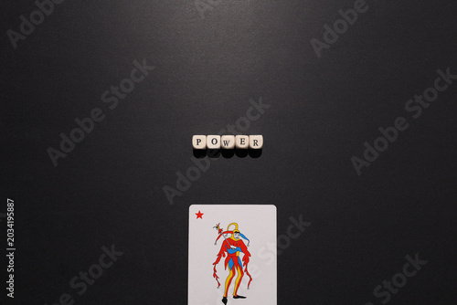 Photos Power spelled with letter tiles above a joker card on dark background, symbolizing control, dominance, leverage and strategic advantage