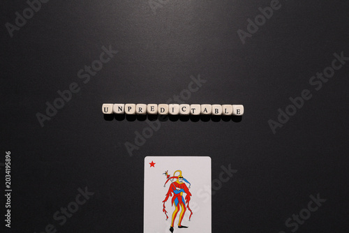 Tableau sur toile Unpredictable spelled with letter tiles above a joker card on dark background, representing uncertainty, volatility, chaos and risk