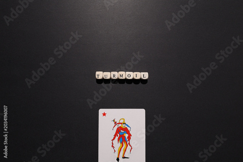 Photos Turmoil spelled with letter tiles above a joker card on dark background, symbolizing chaos, instability, uncertainty and crisis