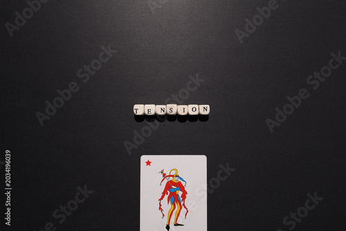 Billede på lærred Tension spelled with letter tiles above a joker card on dark background, representing pressure, uncertainty, rivalry and risk