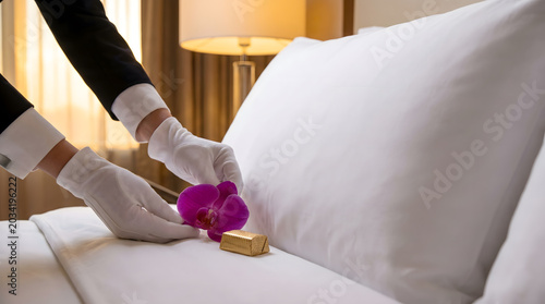 Gloved hands placing orchid and chocolate on hotel bed.