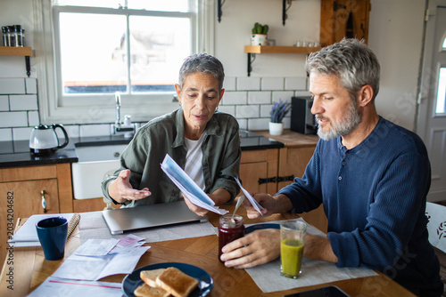 Mature couple reviewing household bills at kitchen table