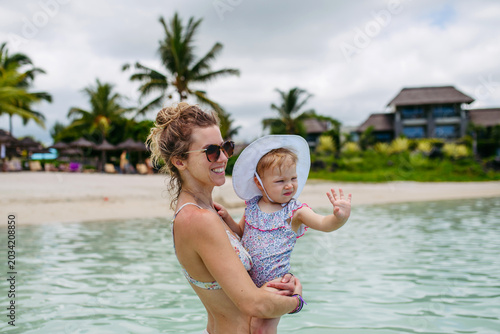 Mother playing in sea water with little daughter.