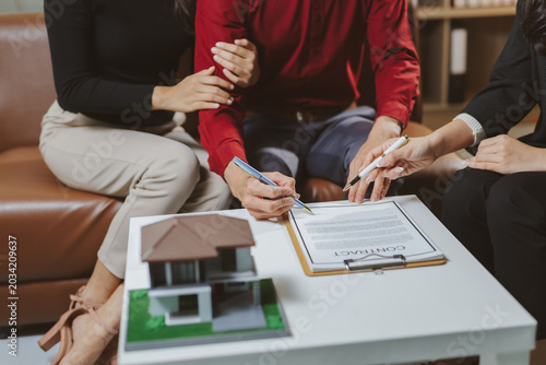 Young couple signing a legal contract for a new house purchase, receiving guidance from a property consultant