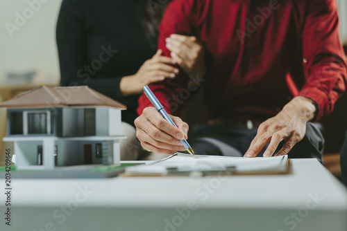 Couple finalizing a home purchase agreement, a man signing documents with a woman reassuring him, symbolizing home ownership and investment